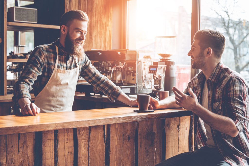 a barista talking to a customer in his coffee shop after serving him